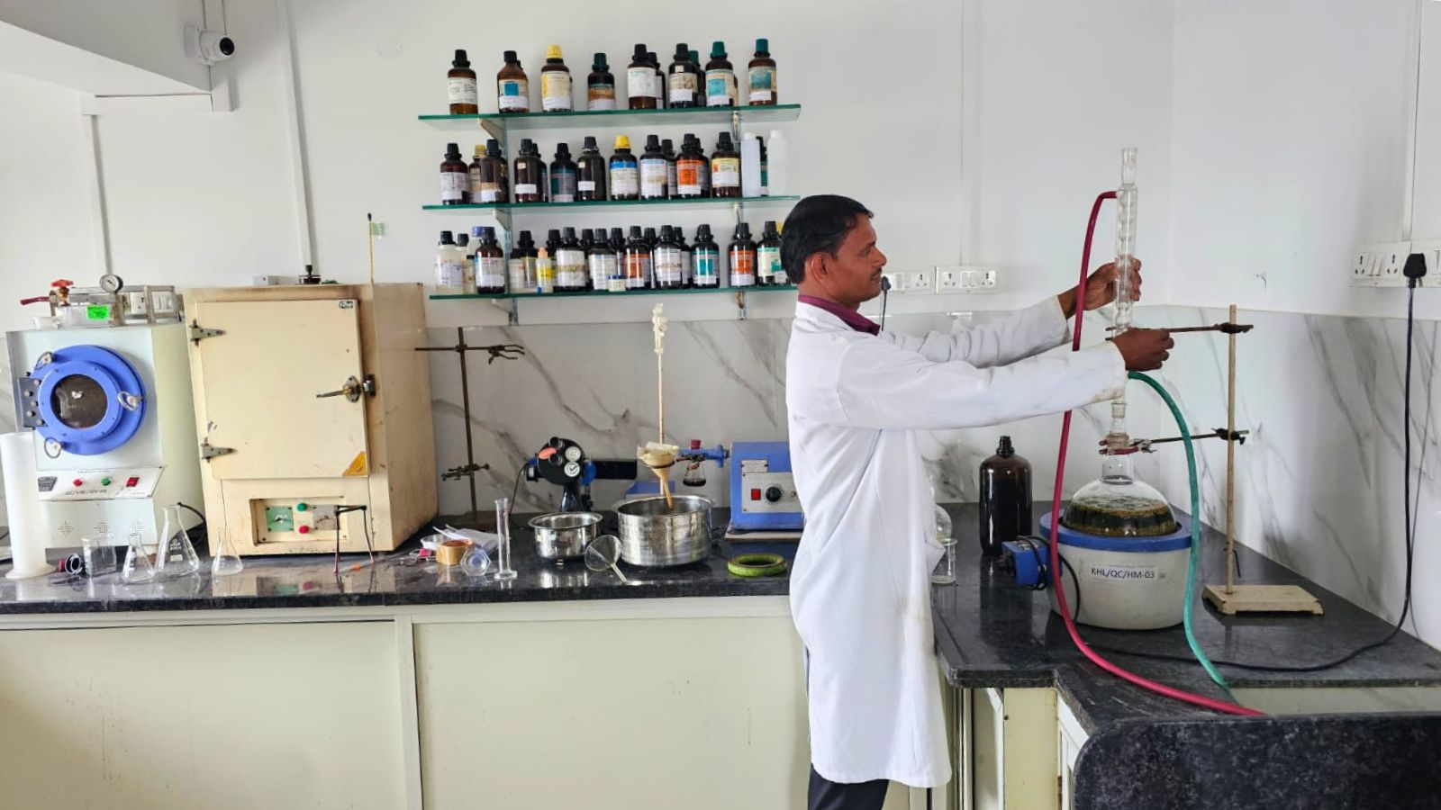 A chemist in a white coat setting up glassware over a heating mantle in the quality control laboratory